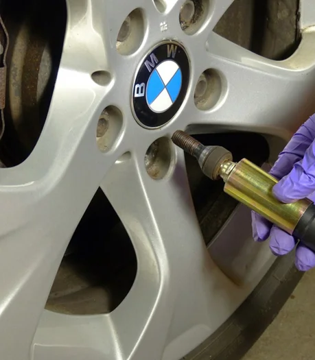 A person wearing gloves applies a torque wrench to a lug bolt on a BMW wheel at Coastal Tyre Services.