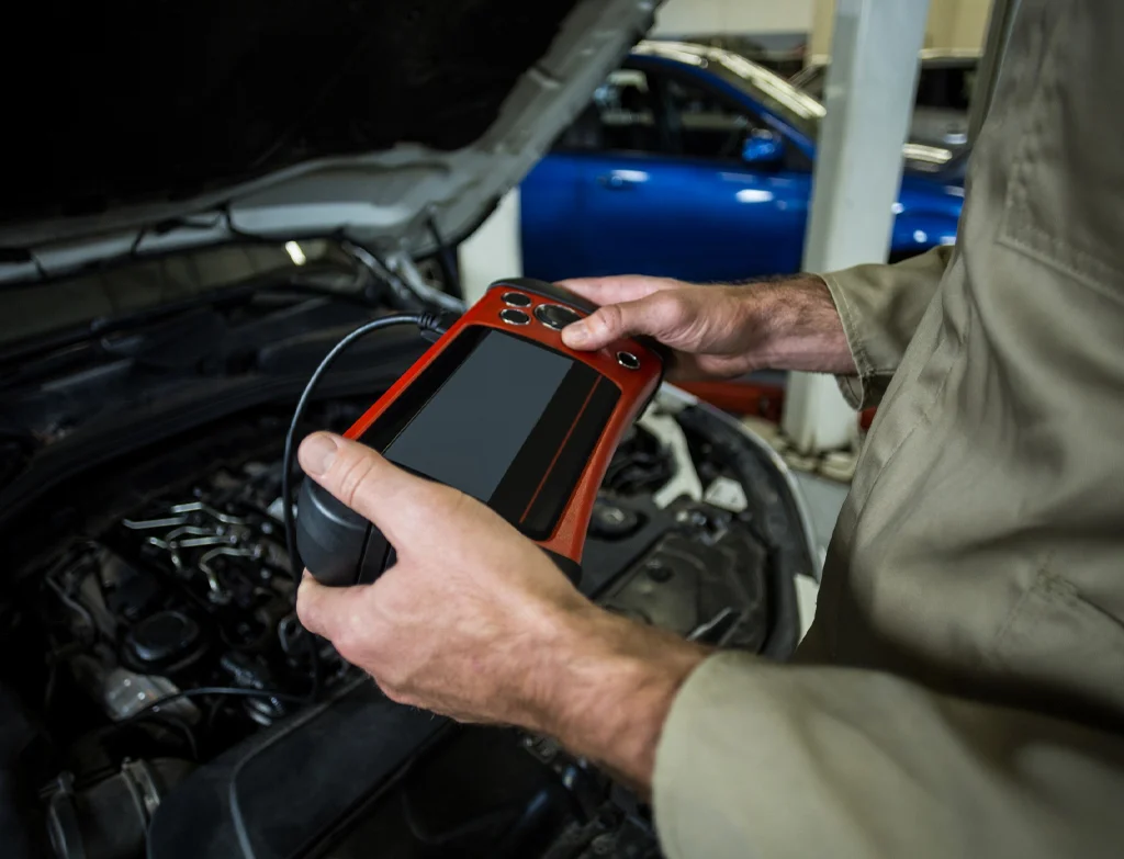 Mechanic in Weymouth holding a diagnostic tool near a car engine.